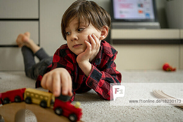 Boy playing with wooden toy train lying on floor at home