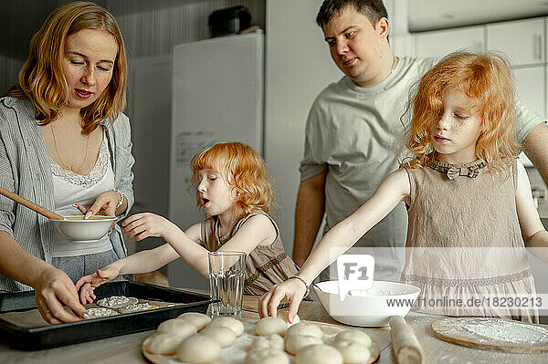 Mutter und Vater bereiten mit ihren Töchtern zu Hause Käsekuchen zu