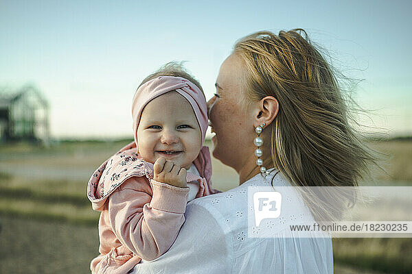 Happy cute baby girl with mother standing in front of sky