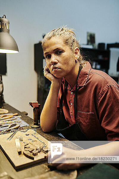 Craftswoman leaning on elbow at workbench in workshop