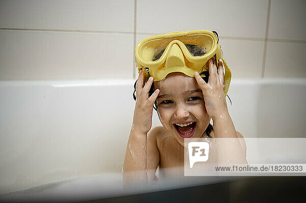 Glücklicher Junge mit Schwimmbrille  der zu Hause im Badezimmer ein Bad nimmt