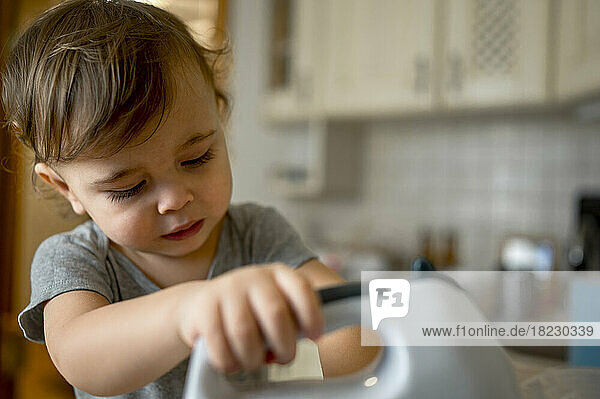 Cute toddler using electric mixer in kitchen at home