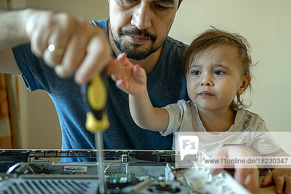 Son looking at father repairing computer at home