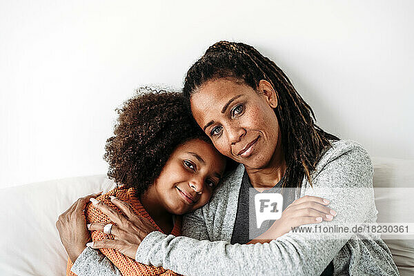 Smiling mature woman hugging daughter on sofa at home