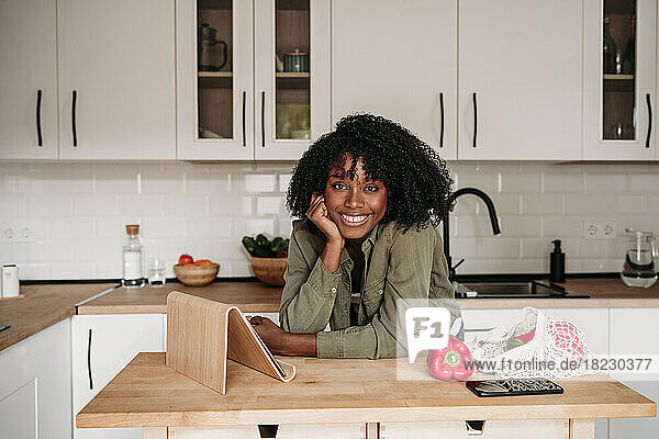 Lächelnde Frau lehnt an einem Tablet-PC auf der Kücheninsel zu Hause
