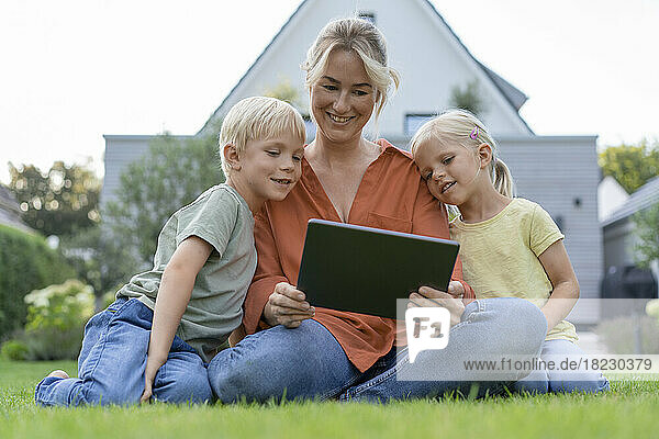 Smiling mother showing tablet PC to children in back yard