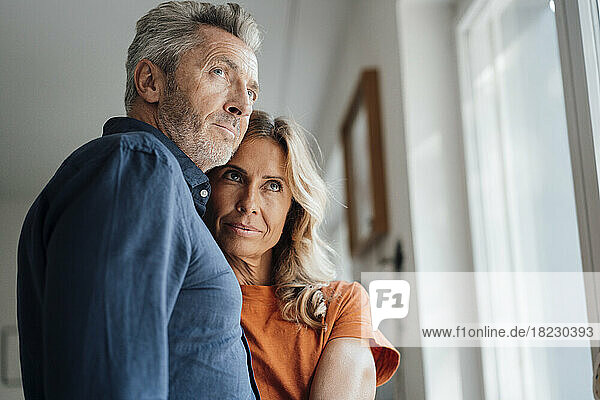 Mature man and woman standing in front of window at home