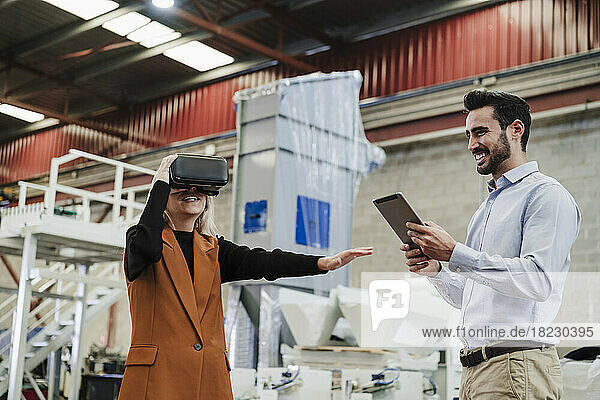 Happy businessman with colleague wearing virtual reality simulator at factory