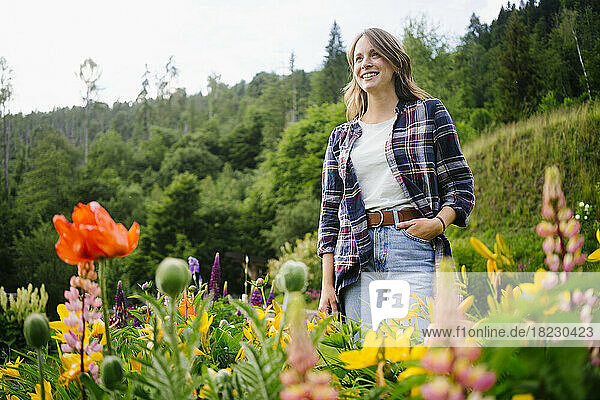 Happy young woman standing amidst flowers in field