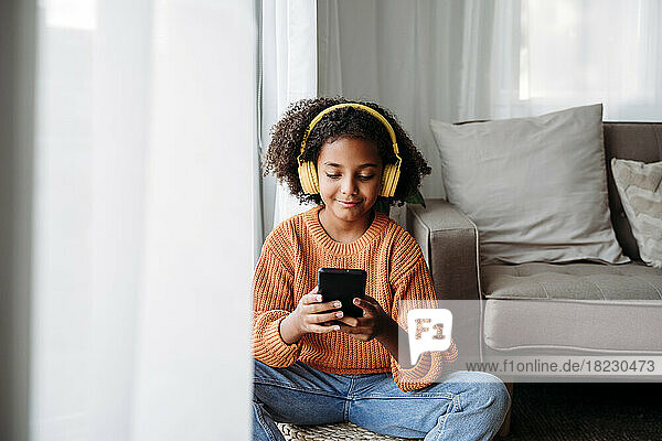 Smiling girl wearing wireless headphones using smart phone at home