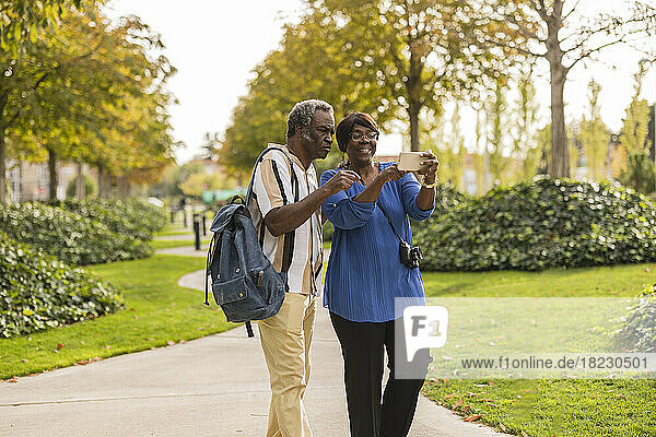 Senior couple using mobile phone standing in park