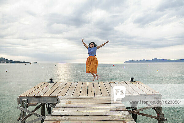 Glückliche Frau springt auf Steg vor dem Meer