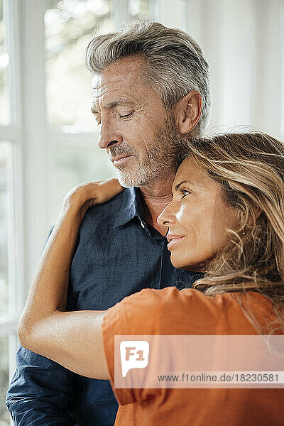 Smiling mature woman embracing man in front of window at home