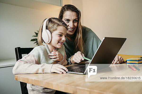 Lächelnde Mutter hilft Tochter beim E-Learning per Laptop auf dem Tisch