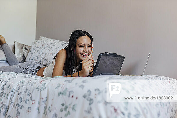 Glückliches Mädchen mit Tablet-PC  das zu Hause im Bett liegt