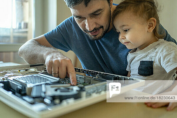 Netter Junge schaut seinem Vater dabei zu  wie er den Computer auf dem Tisch repariert