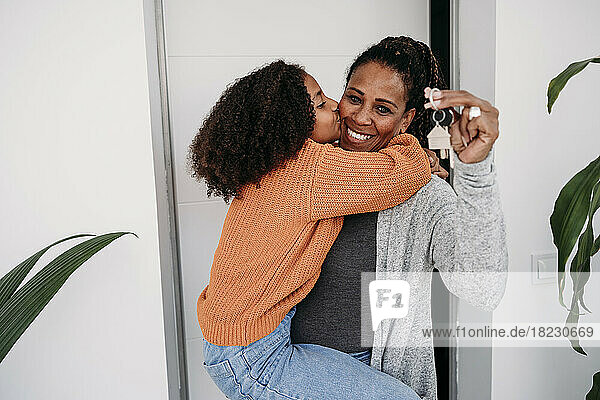 Happy girl embracing mother holding keys of new house