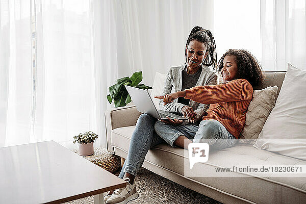 Smiling mother and daughter using laptop on sofa at home