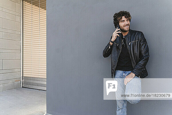 Lächelnder Mann  der vor einer grauen Wand mit dem Mobiltelefon spricht