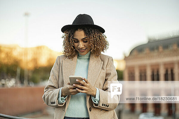 Smiling woman wearing hat using smart phone