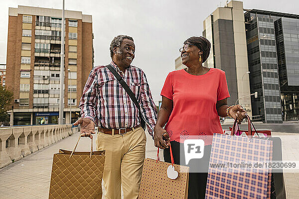 Glückliches älteres Paar  das mit Einkaufstüten auf dem Fußweg läuft
