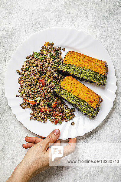 Hand of woman picking up plate of carrot and spinach terrine with lentil salad