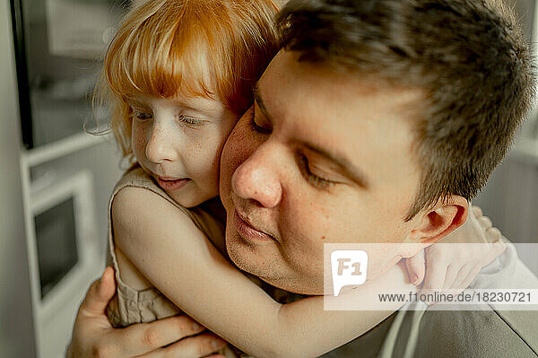 Man with eyes closed hugging daughter at home