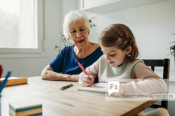 Grandmother helping girl in study on table at home
