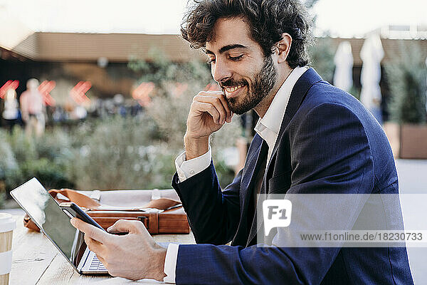 Smiling businessman with hand on chin using smart phone