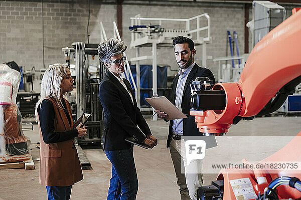 Engineers discussing over robotic arm in industry