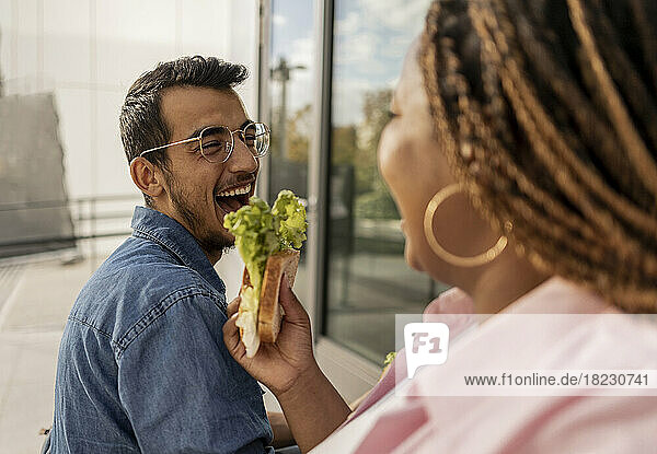 Glückliche junge Frau teilt Sandwich mit Mann am Fußweg