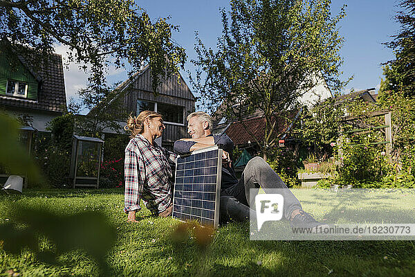 Mature couple sitting with solar panel on grass in back yard