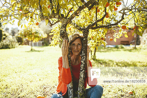 Smiling mature woman sitting under orange fruit tree