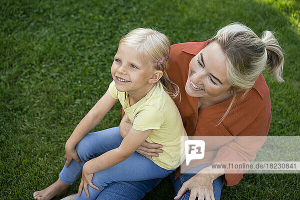 Smiling mother with daughter sitting on grass