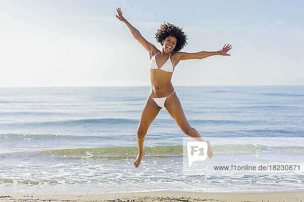 Cheerful young woman jumping in front of sea on sunny day
