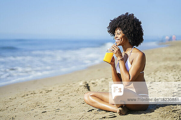 Glückliche Frau trinkt im Sommer Orangensaft am Strand