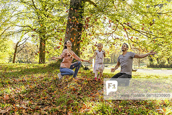 Smiling parents with daughter throwing autumn leaves in park
