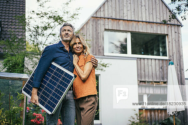 Mature couple standing with solar panel in front of house