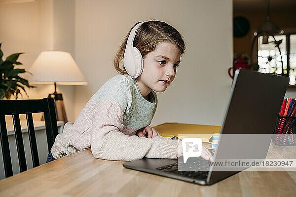 Mädchen trägt kabellose Kopfhörer und benutzt Laptop auf dem heimischen Tisch