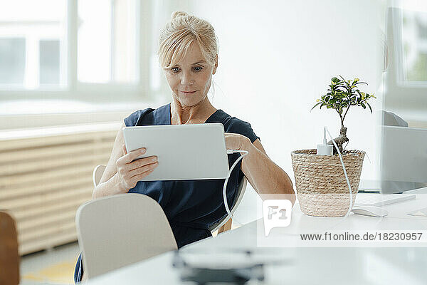 Businesswoman using tablet PC charging through potted plant at office
