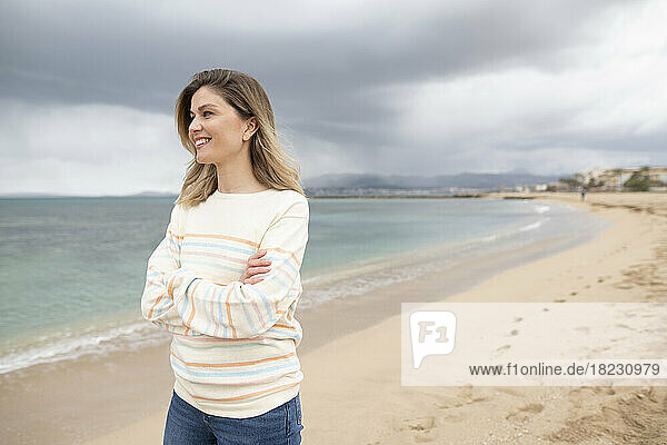 Nachdenklich lächelnde Frau mit verschränkten Armen  die am Strand spaziert