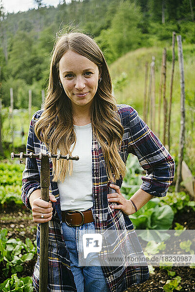 Smiling woman standing with rake in vegetable garden