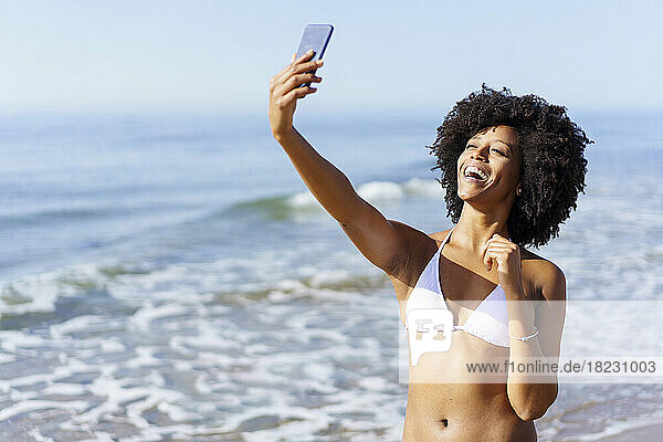 Happy young woman taking selfie through smart phone on sunny day