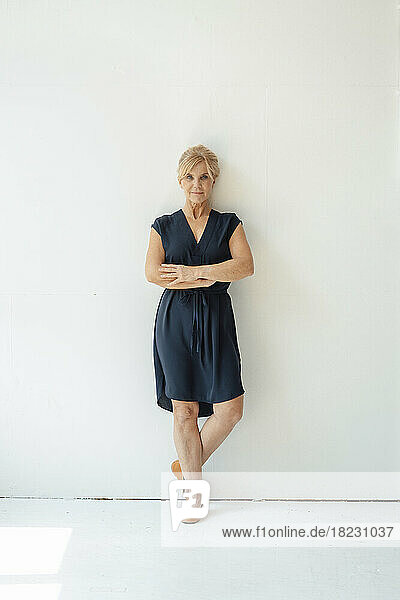 Confident businesswoman with arms crossed in front of white wall