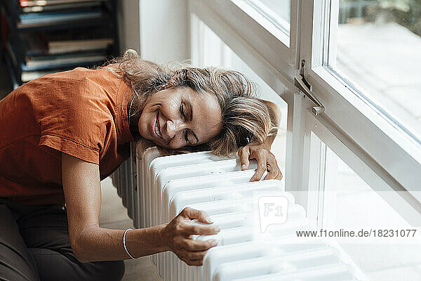 Happy mature woman leaning on radiator at home