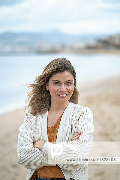 Smiling beautiful young woman with arms crossed standing at beach
