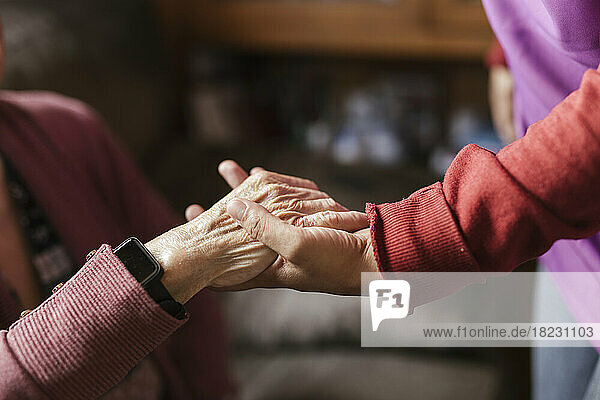 Caregiver holding senior woman's hand at home