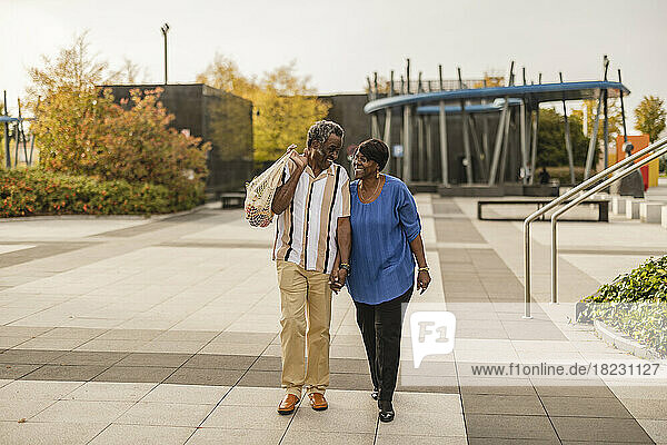 Glückliches älteres Paar hält sich an den Händen und geht auf dem Fußweg