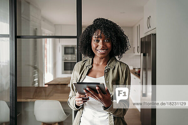 Smiling woman with tablet PC standing by sliding door at home