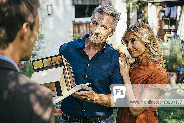 Smiling mature couple having discussion over model house with real estate agent